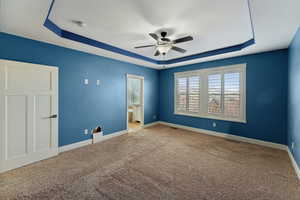 Empty room featuring a tray ceiling, ceiling fan, and carpet floors