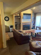 Living room with carpet flooring, built in shelves, and a tile fireplace