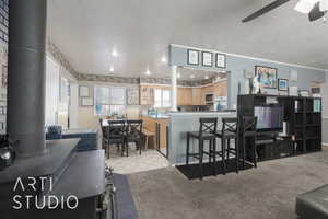 Kitchen with a breakfast bar area, ceiling fan, light colored carpet, and a textured ceiling