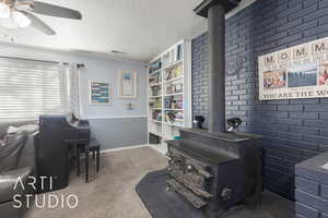 Miscellaneous room featuring a wood stove, ceiling fan, built in features, a textured ceiling, and carpet