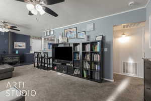 Carpeted living room featuring a wood stove, ceiling fan, a textured ceiling, and ornamental molding