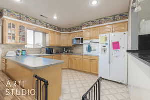 Kitchen with sink, tasteful backsplash, kitchen peninsula, white appliances, and light brown cabinetry