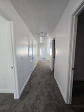 Hallway featuring dark colored carpet and a textured ceiling