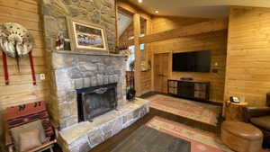 Living room with dark hardwood / wood-style floors, vaulted ceiling, wooden walls, and a stone fireplace