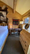 Carpeted bedroom with vaulted ceiling with beams and wooden walls