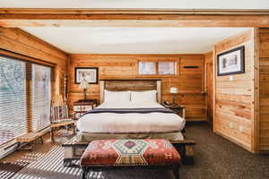 Bedroom featuring dark colored carpet, beam ceiling, and wood walls