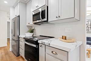 Kitchen with light stone counters, light hardwood / wood-style flooring, white cabinets, and stainless steel appliances