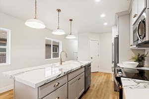 Kitchen featuring a center island with sink, sink, hanging light fixtures, light wood-type flooring, and stainless steel appliances