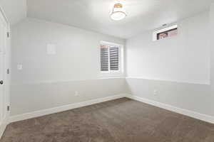 Carpeted spare room featuring vaulted ceiling