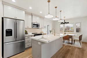 Kitchen featuring a kitchen island with sink, decorative light fixtures, light stone counters, white cabinetry, and stainless steel appliances