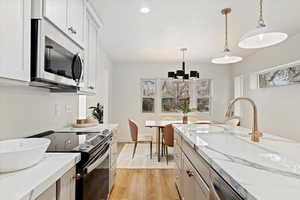 Kitchen featuring stainless steel appliances, sink, decorative light fixtures, a notable chandelier, and white cabinetry