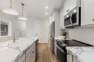 Kitchen featuring appliances with stainless steel finishes, sink, pendant lighting, light hardwood / wood-style flooring, and white cabinetry