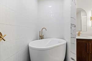 Bathroom featuring vanity, a tub to relax in, and tile walls