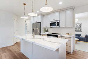 Kitchen with light stone countertops, stainless steel appliances, hanging light fixtures, and an island with sink