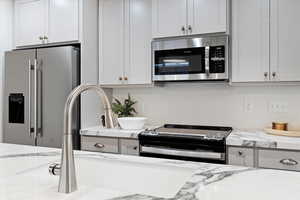 Kitchen with light stone counters, white cabinetry, and stainless steel appliances