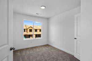 Empty room featuring dark carpet and a textured ceiling