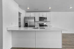 Kitchen with sink, a textured ceiling, white cabinetry, kitchen peninsula, and stainless steel appliances