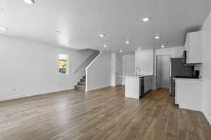 Kitchen featuring hardwood / wood-style floors, a kitchen island with sink, a textured ceiling, appliances with stainless steel finishes, and white cabinetry