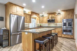 Kitchen featuring sink, a kitchen breakfast bar, appliances with stainless steel finishes, a kitchen island, and light wood-type flooring