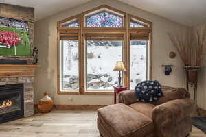 Living area featuring light wood-type flooring, a stone fireplace, plenty of natural light, and vaulted ceiling