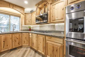 Kitchen with sink, light wood-type flooring, tasteful backsplash, stone countertops, and stainless steel appliances