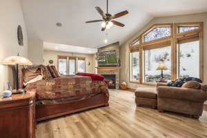 Bedroom with ceiling fan, a fireplace, light hardwood / wood-style floors, and vaulted ceiling