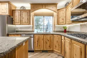 Kitchen featuring light wood-type flooring, sink, appliances with stainless steel finishes, and dark stone counters