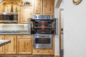 Kitchen featuring decorative backsplash, appliances with stainless steel finishes, light brown cabinetry, and dark stone countertops