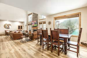 Dining space with a healthy amount of sunlight, a fireplace, a towering ceiling, and light hardwood / wood-style floors