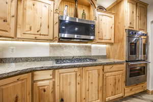 Kitchen featuring light stone countertops, appliances with stainless steel finishes, light wood-type flooring, backsplash, and light brown cabinets