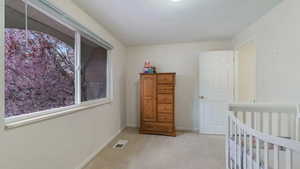 Bedroom with multiple windows, light colored carpet, and a nursery area