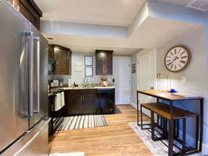 Downstairs Kitchen featuring light stone countertops, light wood-type flooring, dark brown cabinets, sink, and black/Stainless appliances