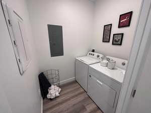 Washroom with electric panel, separate washer and dryer, and light hardwood / wood-style flooring