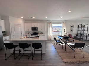 Kitchen featuring appliances with stainless steel finishes, a breakfast bar, a kitchen island with sink, wood-type flooring, and white cabinetry