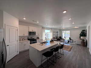 Kitchen with sink, a kitchen island with sink, a breakfast bar, white cabinets, and appliances with stainless steel finishes