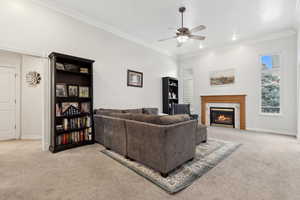 Living room with ceiling fan, light colored carpet, a premium fireplace, and ornamental molding