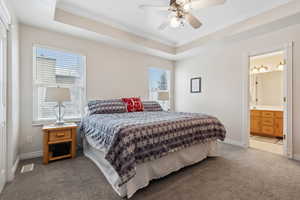 Carpeted master bedroom with ceiling fan, ensuite bath, crown molding, and a tray ceiling