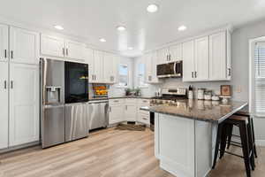 Kitchen with kitchen peninsula, appliances with stainless steel finishes, dark stone counters, white cabinets, and a breakfast bar area