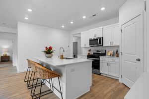 Kitchen featuring a center island with sink, white cabinets, sink, appliances with stainless steel finishes, and a breakfast bar area