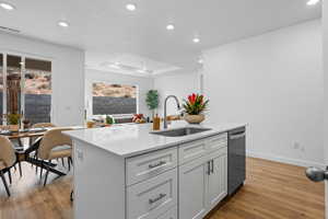 Kitchen featuring a kitchen island with sink, sink, hardwood / wood-style flooring, stainless steel dishwasher, and a tray ceiling