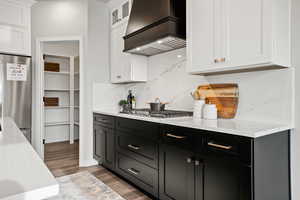 Kitchen featuring white cabinets, light stone counters, appliances with stainless steel finishes, and custom exhaust hood