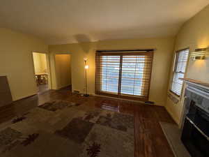 Unfurnished living room with dark hardwood / wood-style floors, lofted ceiling, a textured ceiling, and a tiled fireplace