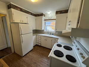 Kitchen with white appliances, white cabinetry, dark wood-type flooring, and sink