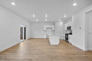 Kitchen featuring a center island with sink, white cabinetry, stainless steel appliances, and light hardwood / wood-style flooring