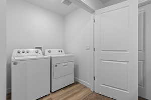 Clothes washing area with washer and clothes dryer and light hardwood / wood-style flooring