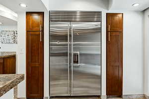 Kitchen with built in refrigerator, dark stone countertops, and recessed lighting