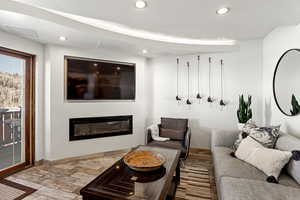 Living room featuring recessed lighting, visible vents, a glass covered fireplace, wood finished floors, and baseboards