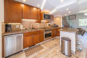 Kitchen with a kitchen bar, black appliances, sink, decorative backsplash, and light stone counters