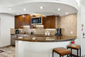 Kitchen with built in microwave, a sink, decorative backsplash, dishwasher, and dark countertops