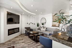 Living area with baseboards, wood finished floors, a glass covered fireplace, and recessed lighting